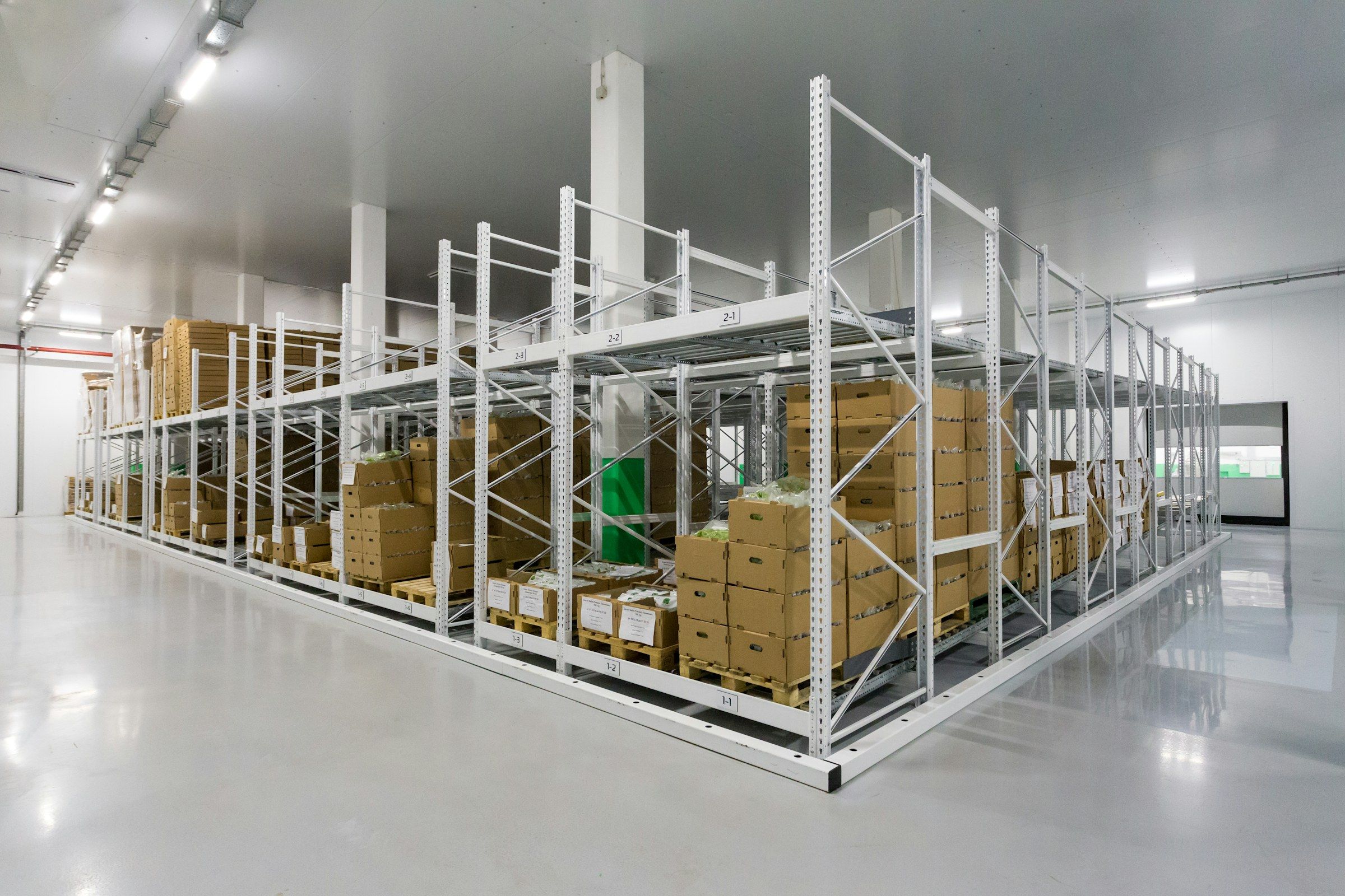 A bright storeroom with white racking and boxed stock on pallets